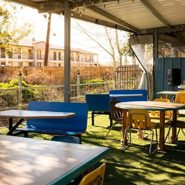 Outdoor patio with blue and yellow tables and chairs on artificial turf under a covered roof.