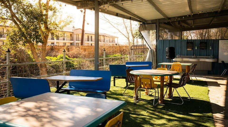 Outdoor patio with blue and yellow tables and chairs on artificial turf under a covered roof.