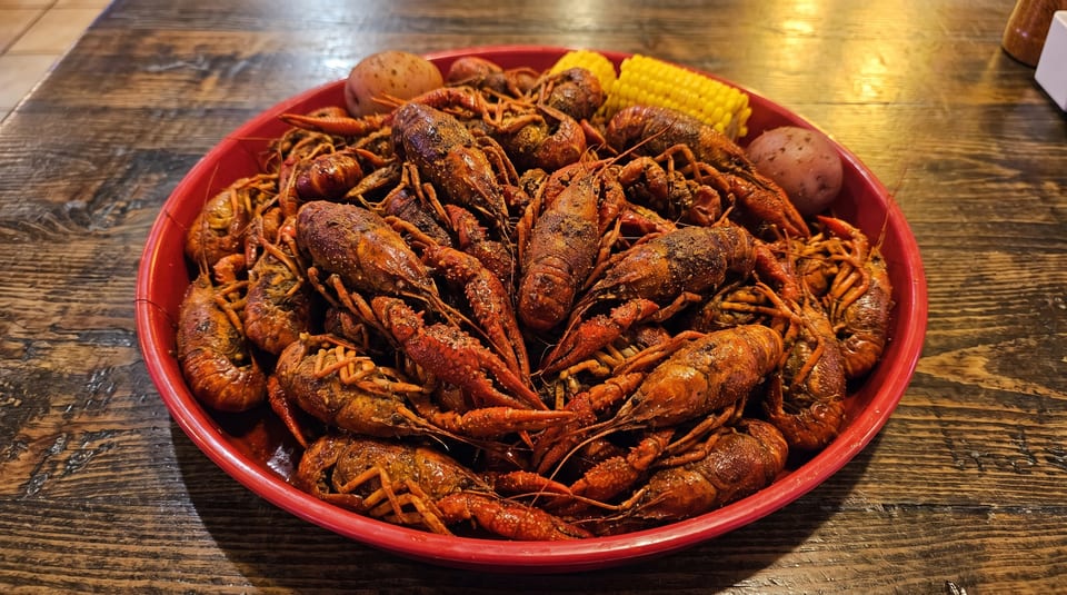 A large red platter overflowing with seasoned crawfish, corn on the cob, and potatoes.
