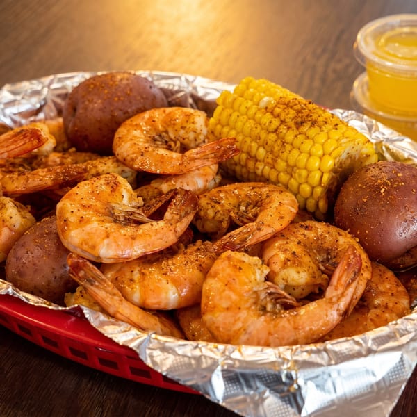 Shrimp boil with corn on the cob and potatoes in a red basket with dipping sauces.