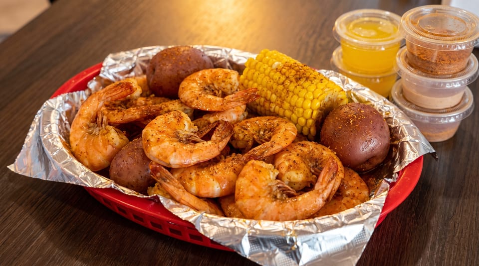 Shrimp boil with corn on the cob and potatoes in a red basket with dipping sauces.