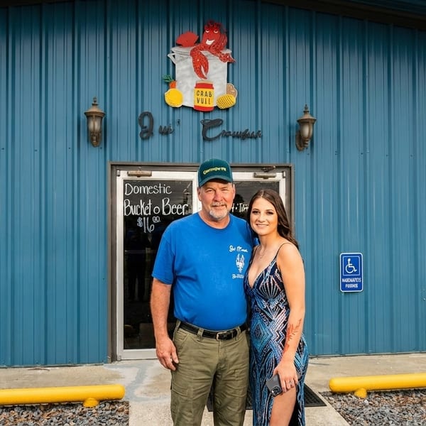 A man and woman stand smiling in front of a blue corrugated metal building with a crab sign.